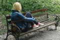 Blonde woman in jeans jacket and pink canvas sneakers sitting on a park bench Royalty Free Stock Photo