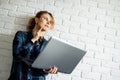 Blonde woman with laptop in her hands standing against white brick wall.