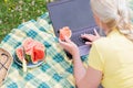 blonde woman with a laptop lies on a blanket in the green grass on a sunny day Royalty Free Stock Photo