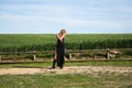 Blonde woman with long hair, young and beautiful dressed in black dress and black boots poses for photos in front of a green wheat Royalty Free Stock Photo