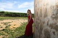 Blonde woman with long hair, young and beautiful, wearing a long red dress and a crown of flowers on her head, leaning against the Royalty Free Stock Photo