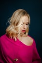 Blonde woman looking down in a pink dress and a golden necklace against a blue background Royalty Free Stock Photo