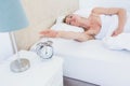 Blonde woman lying in bed reaching for alarm clock Royalty Free Stock Photo
