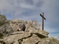 A blonde woman and a man with a backpack admire the mountains in Werdenfelser Land next to a simple wooden puritanical cross
