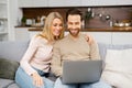 Blonde woman and man looking at the laptop screen while sitting on the sofa and watching comedy movies. Overjoyed couple Royalty Free Stock Photo