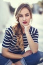 Blonde woman, model of fashion, sitting in urban background.