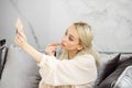 A blonde woman paints lips with beige lipstick. Small mirror in hand Royalty Free Stock Photo