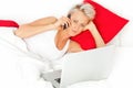 Blonde woman on the phone with a laptop in a bed