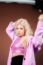 A blonde woman in a pink jacket, a jacket in sequins poses in the studio on a brown background. High fashion, 90s 80s. The girl Royalty Free Stock Photo