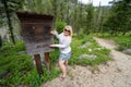 Blonde woman poses near a sign for campers and hikers to register - Please Register Here - at a campground in the Sawtooth