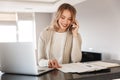 Blonde woman posing sitting indoors at home using laptop computer talking by mobile phone Royalty Free Stock Photo