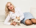 Blonde woman with puppy husky dog on a white sofa. girl playing with a dog