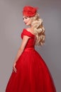 Blonde woman in red dress andBlonde woman in red dress and elegant hat isolated on studio grey background. Beautiful blond girk w Royalty Free Stock Photo