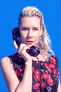 Blonde woman in red dress with retro black phone on blue background Royalty Free Stock Photo