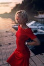 A blonde woman in a red dress stands on the pier. Royalty Free Stock Photo