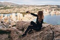 Blonde woman seated on stone rock posing makes selfie picture use phone capture moment climbed up on Penon de Ifach rock in Royalty Free Stock Photo