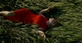 Blonde woman in sensual red dress is lying on rye in field in summer, and relaxing under sun Royalty Free Stock Photo