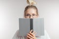 Blonde woman with shocked eyes hiding behind an open book and looking at camera. Royalty Free Stock Photo