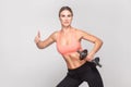 Blonde woman showing like sign and holding dumbbell. Royalty Free Stock Photo