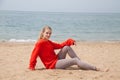 Beautiful blonde woman sits on an empty beach by the ocean Royalty Free Stock Photo
