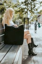 Blonde woman sitting on a bench in a city with a black textile handbag