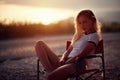 Blonde woman sitting on camping chair and posing. Outdoors relaxation. Camping, outdoors, roadtrip, nature concept
