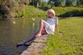 Pretty dreaming young woman sitting near lake in summer park in a warm sunny day. blonde woman sitting near pond