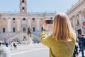 Blonde Woman with smartphone is walking on a sunny day. Capitol in Rome, Piazza del Campidoglio in Capitoline Hill, Rome Royalty Free Stock Photo