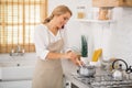 Blonde woman stirring something in a saucepan and talking on the phone