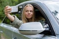 Blonde woman stoped car on road to take a selfie photo. Young tourist explore local travel making candid real moments Royalty Free Stock Photo