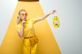 Blonde woman in sunglasses gesturing and holding vintage lamp on white and yellow Royalty Free Stock Photo