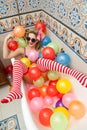 Blonde woman with sunglasses playing in her bath tube with bright colored balloons. Sensual girl with white red striped stockings Royalty Free Stock Photo