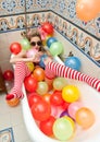 Blonde woman with sunglasses playing in her bath tube with bright colored balloons. Sensual girl with white red striped stockings Royalty Free Stock Photo