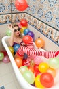 Blonde woman with sunglasses playing in her bath tube with bright colored balloons. Sensual girl with white red striped stockings Royalty Free Stock Photo