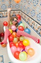 Blonde woman with sunglasses playing in her bath tube with bright colored balloons. Sensual girl with white red striped stockings