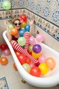 Blonde woman with sunglasses playing in her bath tube with bright colored balloons. Sensual girl with white red striped stockings Royalty Free Stock Photo