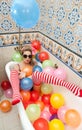 Blonde woman with sunglasses playing in her bath tube with bright colored balloons. Sensual girl with white red striped stockings Royalty Free Stock Photo