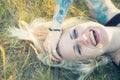 Blonde woman with tattoos and braces laughing in the grass
