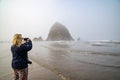 Blonde woman tourists takes photos with her phone of Haystack Rock in Cannon Beach Oregon Royalty Free Stock Photo