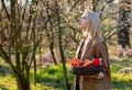 Blonde woman with vegetables in basket in blooming garden