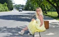 Blonde woman waits by road with suitcase