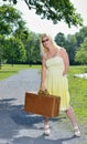 Blonde woman waits by road with suitcase