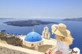 Blonde woman watching view of Santorini near three bells of Fira church in Fira, Santorini, Greece