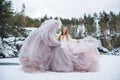 Blonde woman in waving dress in winter outdoors. Fabric flying and fluttering. Fashion model in long waving gown dancing on frozen Royalty Free Stock Photo