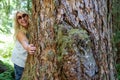 Blonde woman wearing sunglasses hugs a tree