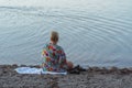 Blonde woman wearing a swimsuit coverup sits on the shores of Lake McDonald