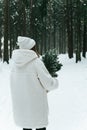 Blonde woman wears white fur coat and knitted hat posing with fir tree in winter forest. Winter fashion Royalty Free Stock Photo