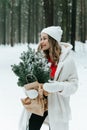 Blonde woman wears white fur coat and knitted hat posing with fir tree in winter forest. Winter fashion Royalty Free Stock Photo