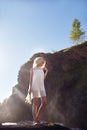 Blonde woman in a white dress and flowers daisies in her hand standing on the rocks near the waterfall. A girl in a light white Royalty Free Stock Photo