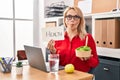 Blonde woman working at the office eating healthy food making fish face with mouth and squinting eyes, crazy and comical